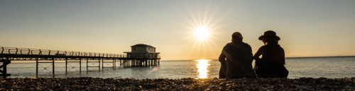 couple watching sunset on the beach next to pier